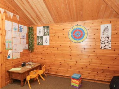 A wooden room with a small wooden table and two yellow chairs with drawings on the walls and a dart board at Bell tent 2 Camerton near Timsbury