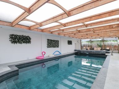 An indoor swimming pool with a wooden beam ceiling and seating area at Bell tent 2 Camerton near Timsbury
