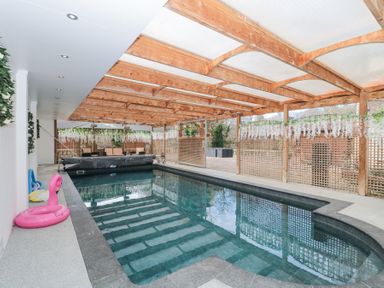 An indoor swimming pool with wooden beams on the ceiling and seating area at Bell tent 2 in Camerton near Timsbury