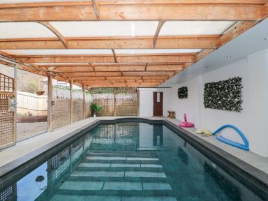 An indoor swimming pool with a wooden beam ceiling and white walls with green wall decor at Bell tent 2 Camerton near Timsbury