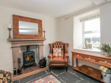 A sitting room with a fireplace and armchair at High Ickenthwaite Farmhouse in Ulverston