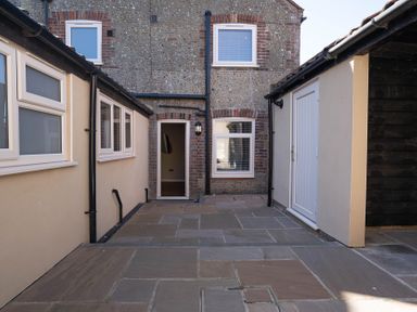 An outdoor patio area with stone flooring between buildings with windows and a door at Driftwood in Kessingland