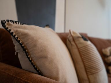 Two cushions on a brown sofa with a white wall in the background at Driftwood in Kessingland