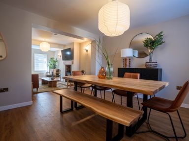 A dining area with a wooden table and bench with chairs and a living room with a TV mounted above a fireplace at Driftwood in Kessingland