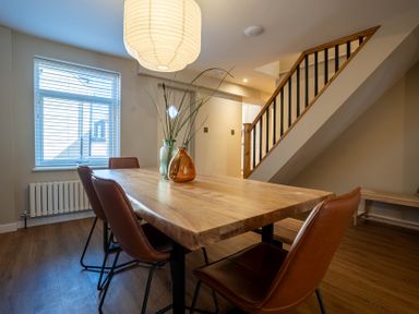 A dining room with a wooden table and brown chairs under stairs at Driftwood in Kessingland