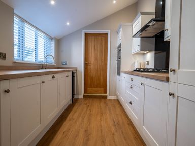 A kitchen with white cabinets wooden countertops a wooden floor and a wooden door at Driftwood in Kessingland