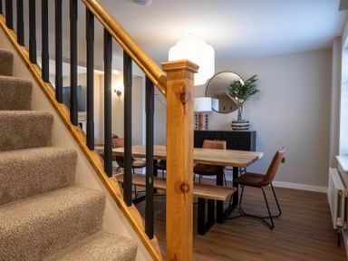 A dining area with a wooden table leather chairs a bench a round mirror a plant and a carpeted staircase at Driftwood in Kessingland