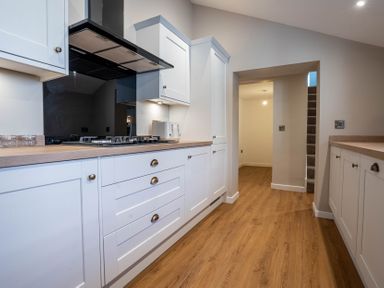 A kitchen with white cabinets and wooden countertops with a gas stove and toaster with wooden floor at Driftwood in Kessingland