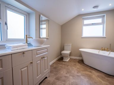 A bathroom with a vanity cabinet with sink and towels a toilet and a freestanding bathtub at Driftwood in Kessingland