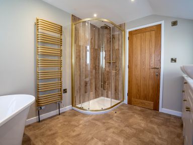 A bathroom with a corner glass shower enclosure wooden door heated towel rail bathtub and a vanity with sink at Driftwood in Kessingland