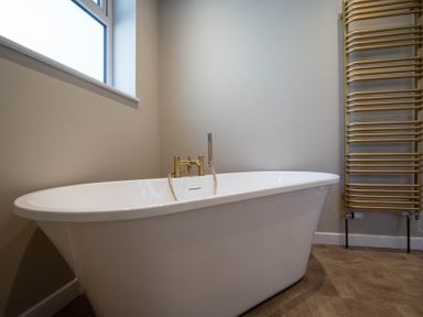 A bathroom with a white freestanding bathtub and a gold towel radiator at Driftwood in Kessingland