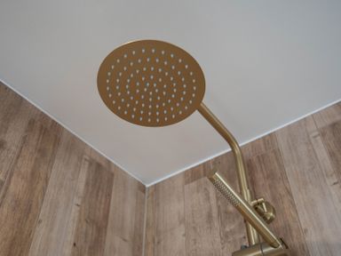 A brass showerhead and handheld shower fixture in a wooden paneled shower at Driftwood in Kessingland
