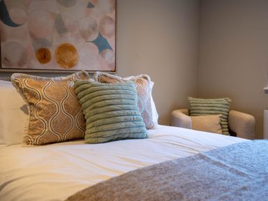 A bed with patterned and ribbed cushions and a chair with cushions in a bedroom at Driftwood in Kessingland