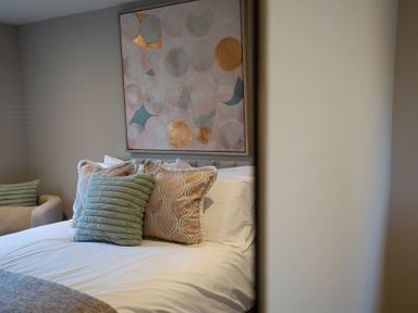 A bedroom with a bed with multiple pillows and a large abstract painting above the headboard at Driftwood in Kessingland