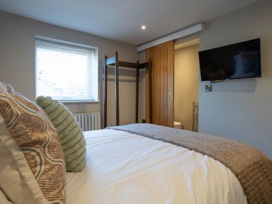 A bedroom with a made bed pillows window wooden clothes rack wall-mounted television and an open door to a bathroom at Driftwood in Kessingland