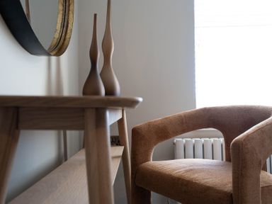 A wooden table with two decorative vases and a brown upholstered chair near a radiator at Driftwood in Kessingland