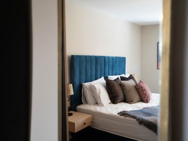 A bedroom with a bed with blue headboard and multiple pillows with bedside tables and lamps at Driftwood in Kessingland