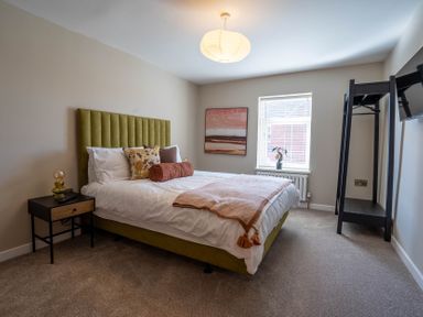 A bedroom with a bed headboard nightstand window and an open clothes rack at Driftwood in Kessingland
