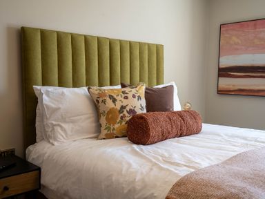A bed with a green upholstered headboard white bedding and decorative pillows in a bedroom at Driftwood in Kessingland