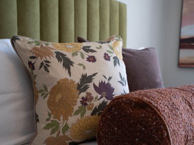 A bed with floral and plain pillows and a textured brown bolster cushion at Driftwood in Kessingland
