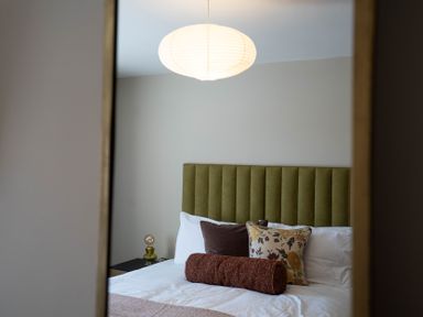 A bedroom with a green upholstered headboard white bedding and decorative pillows at Driftwood in Kessingland