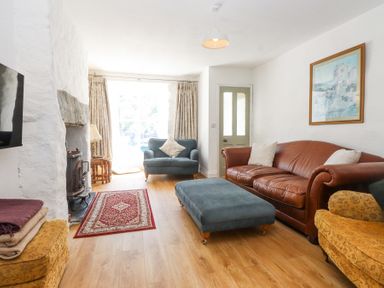 A living room with a leather sofa blue armchair and ottoman a fireplace and framed art at Llys Emrys in Beddgelert