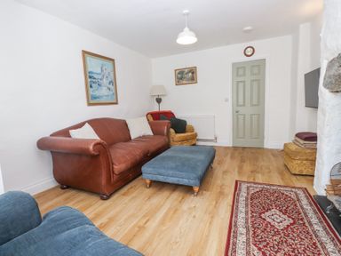 A living room with a brown leather sofa blue ottoman armchair and a red patterned rug at Llys Emrys in Beddgelert