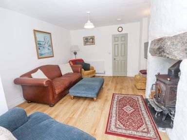 A living room with a leather sofa blue ottoman wood burning stove and artwork on the walls at Llys Emrys in Beddgelert