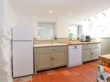 A kitchen with white refrigerator dishwasher sink countertop with coffee maker and kettle at Llys Emrys in Beddgelert