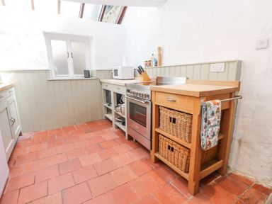 A kitchen with terracotta floor tiles a stove microwave knife block and wicker baskets at Llys Emrys in Beddgelert