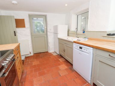 A kitchen with a stove wooden countertops a white dishwasher a white refrigerator a sink and a door at Llys Emrys in Beddgelert