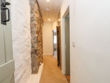 A narrow hallway with exposed stone wall and carpeted floor at Llys Emrys in Beddgelert