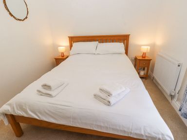 A bedroom with a wooden double bed white bedding two bedside tables with lamps and a wall mirror at Llys Emrys in Beddgelert