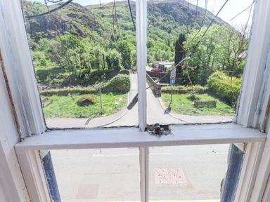 A view of a road park benches and green hillside seen through a window at Llys Emrys in Beddgelert
