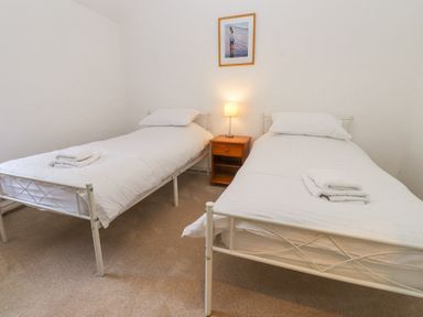 A bedroom with two single beds a wooden bedside table and a lamp at Llys Emrys in Beddgelert