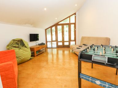 A recreational room with a foosball table bean bag chair wall mounted television and wooden doors at Llys Emrys in Beddgelert
