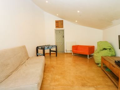 A sitting room with a beige sofa a foosball table an orange sofa a green bean bag and a wooden TV stand at Llys Emrys in Beddgelert