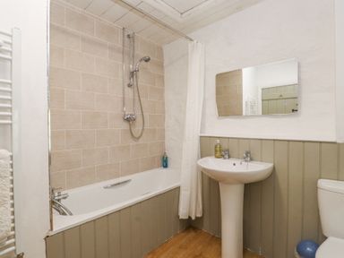 A bathroom with a bathtub shower combination a pedestal sink a mirror and a toilet at Llys Emrys in Beddgelert