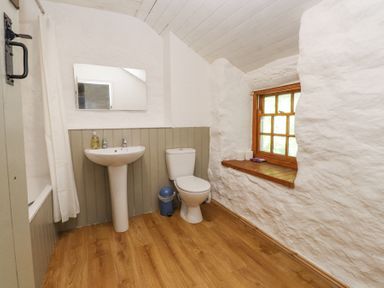 A bathroom with a pedestal sink a toilet a window with wooden frame and a tub with curtain at Llys Emrys in Beddgelert