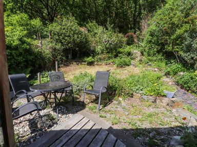 A garden area with outdoor chairs and a round table surrounded by trees and plants at Llys Emrys in Beddgelert