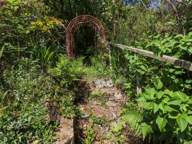 A garden path with stone steps surrounded by plants and a metal archway at Llys Emrys in Beddgelert