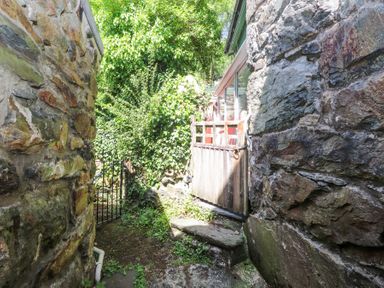 A narrow outdoor passage with stone walls wooden gate and green plants at Llys Emrys in Beddgelert