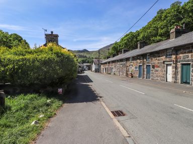 A street with stone cottages on one side and bushes on the other at Llys Emrys in Beddgelert