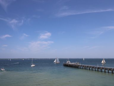 A view of a large body of water with a wooden pier and several sailboats on the water at Plimoth N8 in Yarmouth