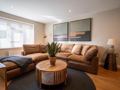 A living room with a brown sectional sofa wooden round coffee table and two abstract paintings at The Reef in Kessingland