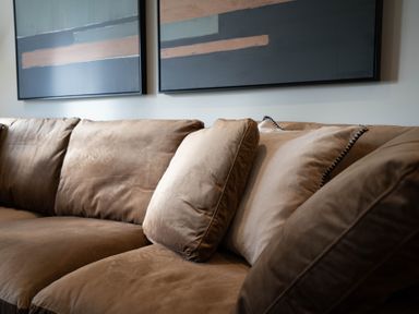 A brown sofa with cushions and abstract paintings on the wall at The Reef in Kessingland