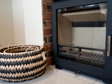 A black metal fireplace with glass door and a woven basket with handles beside it at The Reef in Kessingland