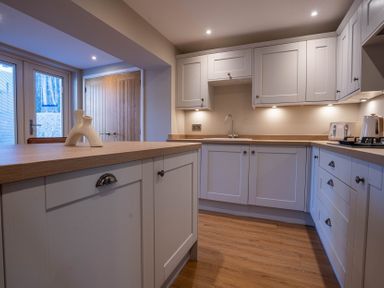 A kitchen with white cabinets wooden countertops a central island and wooden doors at The Reef in Kessingland