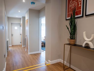 A hallway with wooden flooring a door at the end and a small table with a plant and decorative sculpture at The Reef in Kessingland