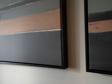 Two framed abstract paintings with horizontal stripes in muted colors on a wall at The Reef in Kessingland